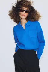 Jersey de punto con cuello tipo polo, manga larga con puños y cierre frontal con botones. Presenta un bolsillo de plastrón en el pecho y diseño de corte holgado.