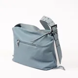 Bandolera celeste de cuero sintético con textura granulada, cierre superior y bolsillo externo con cremallera. Asa de hombro ancha con apliques metálicos.