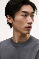 Remera de manga larga color gris oscuro, confeccionada en punto de algodón de peso medio. Presenta cuello redondo acanalado, hombros caídos, puños acanalados y bajo recto. Tiene un corte holgado.