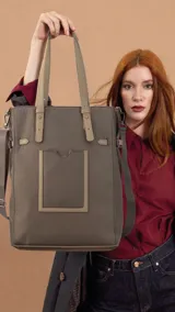 Cartera tipo tote de diseño vertical, color verde oliva, con doble asa superior y correa ajustable extraíble. Presenta un bolsillo frontal plano con detalle de ribete en color contrastante.