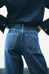 Jeans de tiro alto, pierna ancha y corte recto, confeccionado en denim de algodón rígido de color azul medio. Presenta un detalle de herrajes metálicos en la cintura.