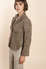 Chaqueta marrón de lana con cuello, solapa y bolsillos ojal. Forro solo en las mangas y terminaciones envivadas. Esquinas redondeadas y mangas con corte en puño que permiten transformarla en manga 3/4. Más larga en la espalda que en la delantera. Abrochadura con dos botones.
