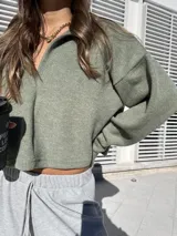 Buzo de tejido suave color verde oliva, con diseño holgado, cuello polo abierto y mangas largas con puños ajustados.