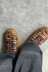 Championes urbanos de diseño bajo, confeccionados en cuero con estampado animal print tipo tigre en tonos marrones y beige. Poseen cordones marrones, suela de goma marrón y costuras visibles en color blanco.