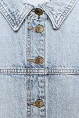 Cazadora de denim en color azul oscuro con costuras en contraste, cuello solapa, manga larga y cierre frontal con botones metálicos. Presenta dos bolsillos de plastrón en el delantero.