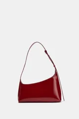 Bolso de hombro rojo de diseño asimétrico en acabado brillante. Cuenta con asa ajustable, bolsillo interior y cierre mediante cremallera metálica.