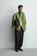 Parka estilo militar color verde, de corte relaxed fit, cuello subido y manga larga. Cuenta con bolsillos de plastrón con solapa en el pecho y en la cadera, cintura ajustable con cordón interior y cierre frontal con cremallera oculta por solapa con botones a presión.