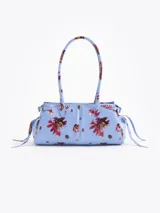 Cartera de hombro de cuero vacuno color celeste con estampado floral multicolor. Cuenta con cierre superior, bolsillo interno, asas largas y detalles de herrajes metálicos con candado y llavero colgante en el frente.