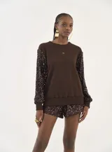 Buzo de cuello redondo color marrón, con mangas largas confeccionadas en tela con lentejuelas brillantes del mismo tono. Presenta puños y ruedo acanalados y un pequeño logo bordado en el centro del pecho.