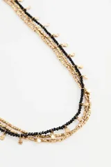 Collar multicapa compuesto por varias cadenas finas que alternan cuentas de vidrio negras y cuentas metálicas doradas, con pequeños dijes colgantes circulares.