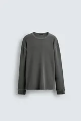 Camiseta de manga larga con cuello redondo, confeccionada en tejido de algodón con textura tipo waffle y efecto lavado. Presenta un corte relajado con puños en rib y bajo irregular.
