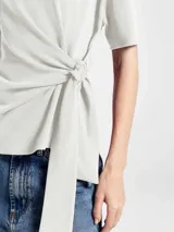 Blusa de algodón color beige, con cuello redondo, mangas cortas y detalle de lazo lateral que genera un efecto drapeado en la cintura.