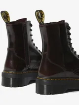 Borcego Dr. Martens modelo Jadon Arcadia, color bordó brillante con efecto desgastado que revela capas contrastantes. Presenta 8 ojales dorados, cordones negros, suela de plataforma de 4 cm con surcos laterales, tirador con logo AirWair y pespunte amarillo.
