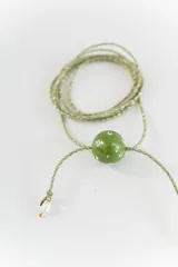 Gargantilla tipo bolo tie de tiento trenzado verde con dije esférico celeste con brillos incrustados.