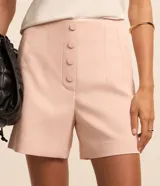 Short de sastrería color rosado, de tiro alto con detalles de pinzas frontales y cartera abotonada con cuatro botones revestidos. Presenta diseño recto y estructurado.
