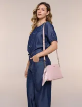 Cartera bandolera estructurada de eco cuero rosado con textura graneada, silueta curva y cierre superior. Posee correa larga regulable con detalles de cadena dorada, bolsillo frontal con logo metálico, pañuelo estampado a contratono anudado en un lateral y base rígida con apoyos metálicos.