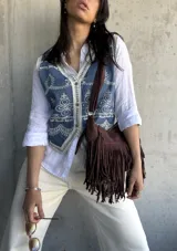 Chaleco de jean azul con bordados florales blancos y ribete de encaje. Cierre frontal con botones.