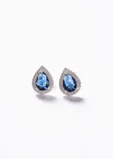 Aros tipo caravanas con diseño de gota, elaborados en plata 925 con una piedra central de zirconia azul rodeada por pequeñas zirconias blancas.