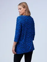 Blusa azul con estampado de círculos negros, de tejido texturado con escote en V descentrado y aplique de aro metálico.