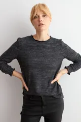 Remera de manga larga con cuello alto tipo media polera, confeccionada en tejido texturado de color beige melange, con puños con detalle de volados.