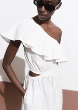 Vestido midi color blanco de diseño evasé y corte asimétrico con un hombro descubierto. Cuenta con un volante grande en el escote, detalles cut-out en la cintura y falda larga y amplia con bolsillos.