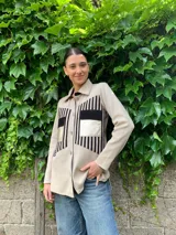 Camisa color beige con detalles de cuero negro en los bolsillos y en la parte superior del frente, de lana merino, con cuello clásico y cierre con botones.