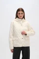 Campera acolchada de color blanco con diseño capitoneado en forma de rombos, manga larga, capucha y cierre frontal con botones a presión dorados.
