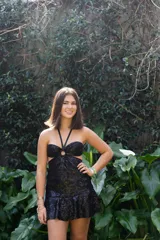 Vestido corto de lentejuelas color ciruela o morado oscuro, con escote corazón y detalle de argolla central que conecta con tirantes finos que atan al cuello. Presenta aberturas laterales (cut-outs) en la zona de la cintura y falda corta con vuelo.