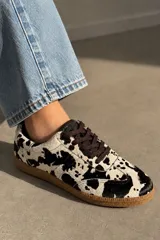 Championes de cuero vacuno con estampado de animal print tipo vaca en tonos blanco y negro, cordones marrones y suela de goma.