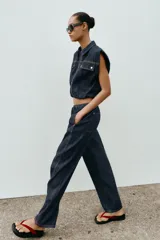 Chaleco de denim oscuro con cuello solapa, cierre frontal con cremallera metálica y bolsillos delanteros con tapeta. Presenta un diseño de corte abullonado con bajo elástico.