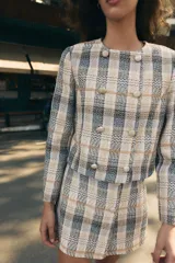 Falda pantalón de tiro alto confeccionada en tejido de tweed con estampado a cuadros en tonos beige, azul y negro. Presenta detalles de falsos botones y cierre lateral con cremallera oculta.
