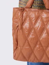 Cartera de eco cuero color marrón, con diseño capitoneado en rombos de gran relieve. Cuenta con un compartimento principal con cierre, amplios bolsillos laterales con botones imantados, asa de mano fija y correa larga regulable y removible. El forro interno es textil a tono con compartimentos organizadores.