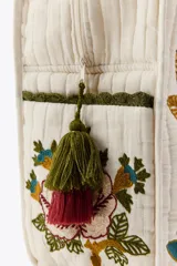 Bolso tote acolchado de color blanco crudo, con asas de hombro y bordados florales grandes y coloridos en tonos rojo, marrón, azul y verde. Presenta un forro interior y cierre de cremallera metálica.