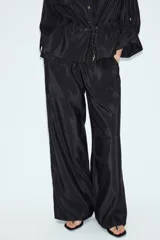 Pantalón de tiro alto color verde militar, confeccionado en tejido satinado con acabado brillante. Presenta cintura elástica fruncida, bolsillos laterales ocultos en las costuras y perneras de corte ancho.