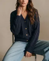 Cardigan de punto texturado en color azul marino, con cuello en V, cierre frontal de botones dorados y bolsillos laterales. Presenta un diseño de tejido con relieve y puños acanalados.