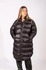 Campera puffer larga de color negro con acabado brillante, cierre frontal con botones a presión y cuello alto. Presenta un parche circular en la manga izquierda.