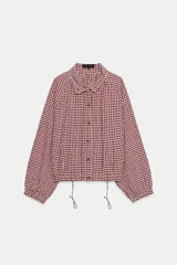 Chaqueta corta con estampado de cuadros vichy en tonos bordó y blanco, cuello camisero, manga larga con puños elásticos y bajo ajustable con cordón fruncido. Cierre frontal con botones.