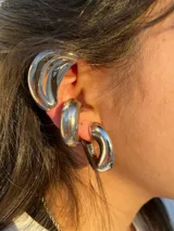 Set de tres piezas de joyería para la oreja, color plateado, con acabado brillante y diseño grueso y orgánico. Incluye un ear cuff que cubre parte de la oreja y dos aros gruesos.