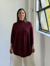 Poncho de punto color bordó con cuello alto y diseño de trenzas verticales en el frente. Presenta mangas tres cuartos con puños acanalados y un corte holgado con ruedo redondeado.