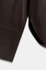 Camisa de cuello solapa y escote en pico, con manga larga y cierre frontal mediante botones. Presenta un diseño fluido con bajo asimétrico y aberturas laterales.