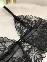 Conjunto de lencería compuesto por un bralette de encaje negro con cierre frontal de gancho y breteles regulables, y una tanga de encaje con tiras elásticas laterales ajustables y argollas metálicas.