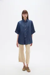 Camisa azul de jean de manga corta, corte holgado, con cuello camisero y cierre frontal con botones.