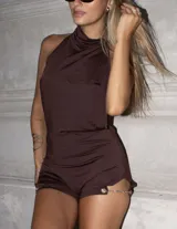 Enterito corto color marrón oscuro, ajustado al cuerpo, con cuello alto y espalda descubierta. Presenta un detalle de cadena metálica en el lateral de la pierna.