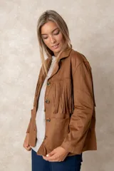 Chaqueta de gamuza sintética color marrón, con diseño de flecos en el pecho y la espalda. Presenta cierre frontal con botones, cuello camisero y bolsillos cuadrados frontales.