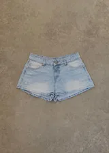 Short de jean tiro bajo color celeste con efecto desgastado, bolsillos traseros y etiqueta de cuero marrón en la cintura.