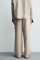 Pantalón de hombre de corte relajado, color beige claro, con cintura elástica, cierre frontal con botón y cremallera, bolsillos delanteros y bolsillos traseros de vivo.