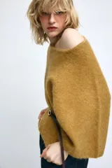 Jersey de punto color mostaza con cuello redondo y mangas amplias tipo murciélago. Presenta un diseño ajustado en la cintura con un cinturón fino de cuero sintético en color marrón a contraste.
