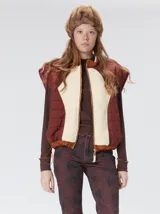 Chaleco de corte cuadrado con diseño bicolor en tonos terracota y crema. Presenta cierre frontal metalizado, parches de nylon en el pecho, interior forrado en corderito y cordón ajustable en el ruedo.