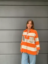 Camisa tejida a rayas horizontales color naranja y blanco, con cuello camisero, mangas tres cuartos y bolsillos frontales con solapa en color dorado.