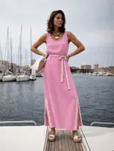 Vestido largo sin mangas color rosado, con escote redondo, bolsillos laterales y detalles de pasamanería en zigzag beige en el cinturón y los tajos laterales.